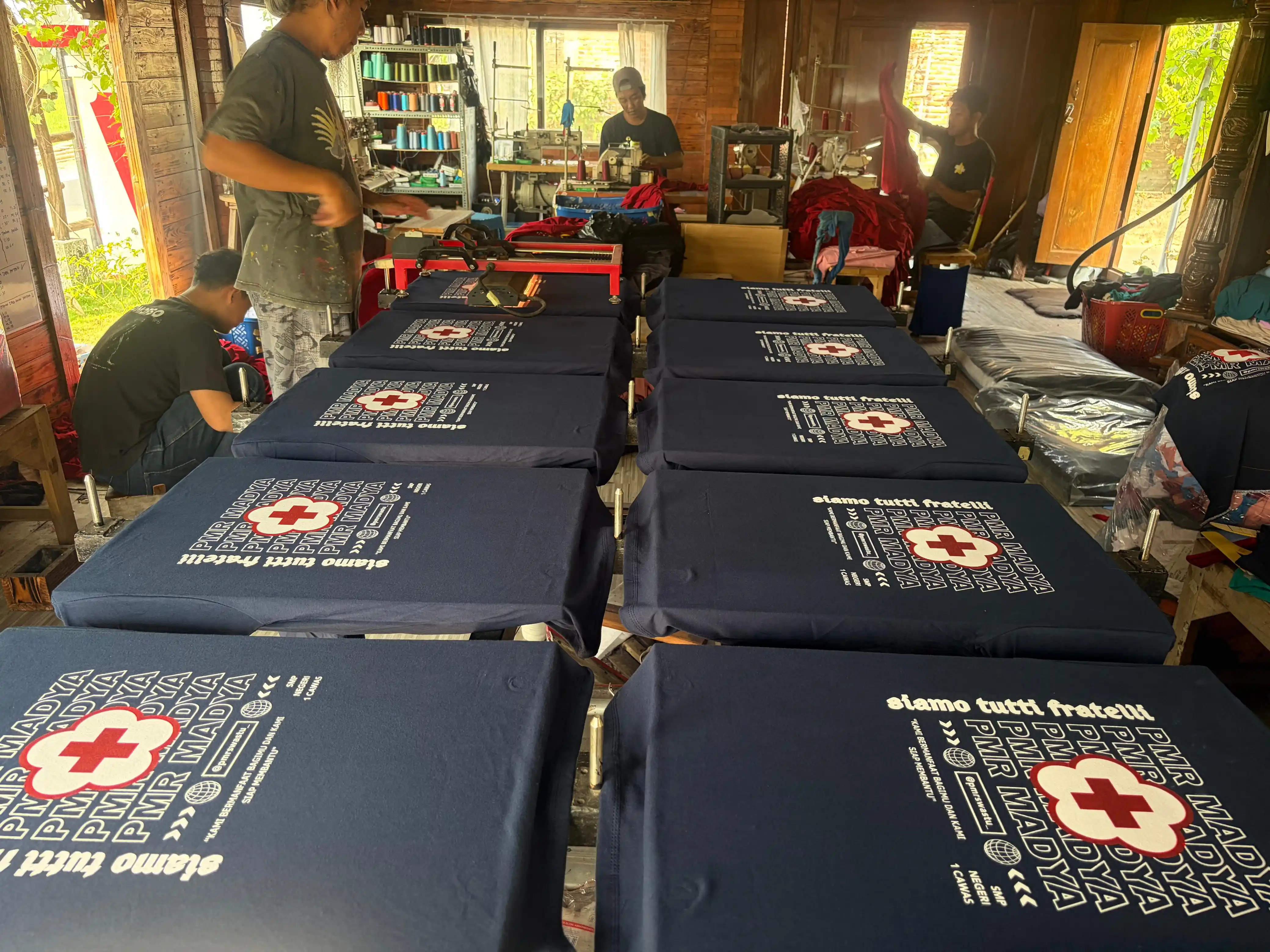 Hasil sablon Kaos PMR Madya SMP Negeri 1 Cawas warna navy tampak depan dan belakang — bagian depan bertuliskan nama dan logo Palang Merah Indonesia, bagian belakang bertuliskan Siamo Tutti Fratelli dan PMR Madya berulang dengan motto Kami Bermanfaat Bagimu dan Kami Siap Membantu